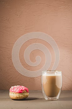 donut in red glaze and a cappuccino/donut in red glaze and cappuccino glass on a brown background with copy space