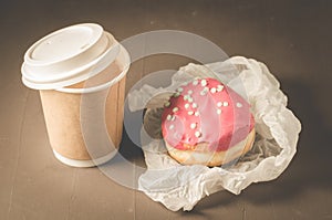 donut in red glaze and a paper coffee cup/donut in red glaze and a paper coffee cup on a dark table