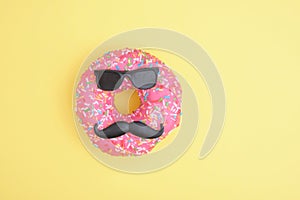 Donut with sprinkles and pink icing, donut with mustache and glasses, fun minimalistic food concept, foodporn, yellow background