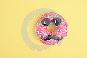 Donut with sprinkles and pink icing, donut with mustache and glasses, fun minimalistic food concept, foodporn, yellow background