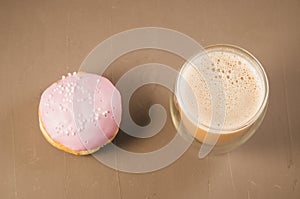 donut in violet glaze and a cappuccino glass/donut in violet glaze and a cappuccino glass on a brown background, top view