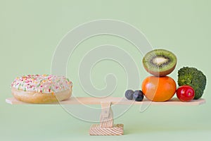 Donut vs. fruits and vegetables on wooden seesaw, diet and calories concept