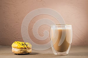 donut in yellow glaze and a cappuccino glass /donut in yellow glaze and a cappuccino glass on a brown background. Selective focus