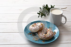 Donuts on a blue plate with a cup of milk on a white wooden background