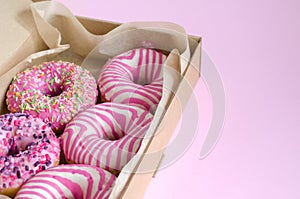 Donuts close-up with pink icing lie in an open box on a pink background. Horizontal background, selective focus