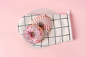 Donuts decorated with icing and topping lie on the chef`s glove on a pink background top view copy