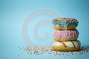 Donuts doughnuts of different colors on a blue background with multi-colored festive sugar sprinkles. Holiday and sweets, baking