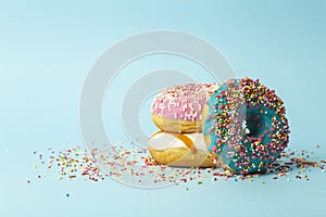 Donuts doughnuts of different colors on a blue background with multi-colored festive sugar sprinkles. Holiday and sweets, baking