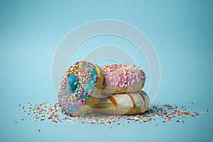 Donuts doughnuts of different colors on a blue background with multi-colored festive sugar sprinkles. Holiday and sweets, baking