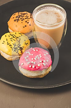 donuts in glazes and a glass of a cappuccino /donuts in glazes and a glass of a cappuccino on a black tray. Selective focus