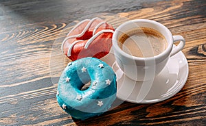 Donuts one with blue icing and white stars and with red icing and white stripes and a cup of coffee on a wooden table
