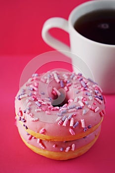 Donuts in pink glaze with sprinkles next to a white cup of coffee