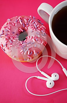 Donuts in pink glaze with sprinkles next to a white cup of coffee and headphones laid out in the shape of a heart