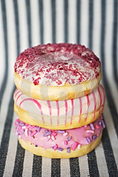 Donuts with pink icing in a column on a striped background
