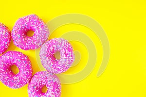 Donuts with pink icing on a yellow background top view. Place for text. Sweets, junk food, pastries. Bright colors
