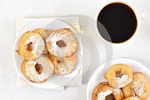 Donuts with powdered sugar on white plate, cup of black coffee