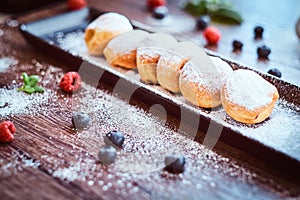 Donuts sprinkled with powdered sugar on a black long plate with raspberry bilberry and mint.