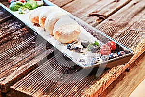 Donuts sprinkled with powdered sugar on a black long plate with raspberry bilberry and mint.