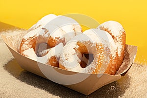 Donuts sprinkled with powdered sugar on a paper plate. Takeout food. Colored background
