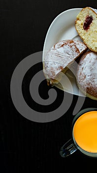 Donuts with sugar on a white plate and black background with jam. Isolated donuts in vertical photo and fresh juice