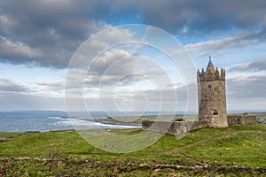 Doonagore Castle on a green hill, Doolin pier and Atlantic ocean in the background. Beautiful cloudy sky. Popular tourist