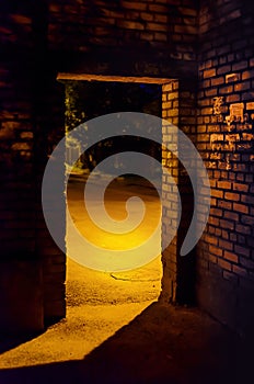 Door arch in a darkened brick wall, behind which a lit street is visible