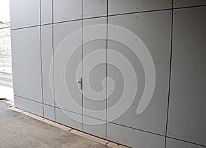 A door without a ball handle leading to a hidden utility room. the door is hard to distinguish from the cladding of the industrial