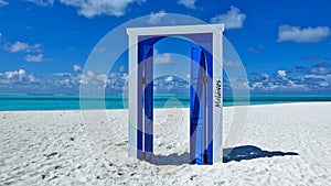 The door is fortunately open. Sunny day, on the white sand of the beach is a blue open door