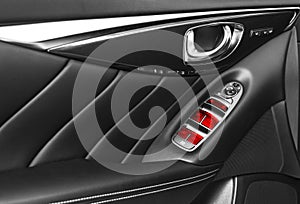 Door handle with red Power window control buttons of a luxury passenger car. Black perforated leather interior with stitching of t