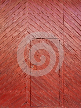 A door inside a huge old patio door of a village house made of red wooden slats