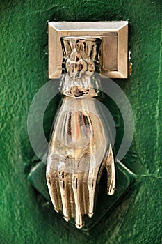 Door knocker with hand shape on green wooden door