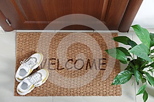 Door mat with word WELCOME and shoes near entrance, top view