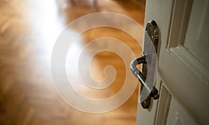 Door open close up. Retro doorknob on white door, blur floor parquet, classy house interior