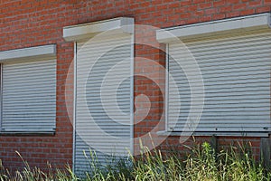 The door and windows are closed by white rolls on a brown brick wall