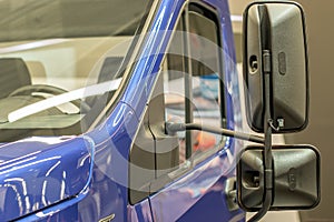 Door, windshield and hood with reflections on it. Front part blue cargo vehicle truck body with rear view mirrors close-up