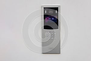 Doorbell with video camera and microphone, on the white wall of an apartment building, doorbell camera