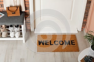 Doormat with word Welcome near shoe rack on white wooden floor in hall