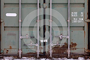 The doors of a large old container are painted in close-up in green with rust, with pipe-type locks and white lettering indicating
