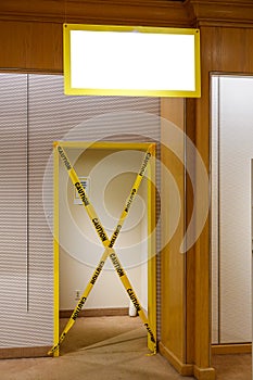 Doorway with yellow trim and caution tape covering the entrance. A blank white sign is over the door.