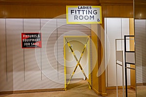 Doorway with yellow trim and caution tape covering the entrance. Sign over the door says that it is the ladies fitting room. A red