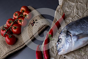 Dorado fish on slate board with cherry tomatoes, lemon, garlic, rosemary, chilly pepper and peppercorns. Top view