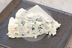 Dorblu cheese with blue and green mold veins on black serving plate