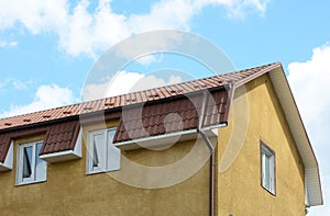 Dormer windows on metal roof. A house with a roof made of metal roofing with mansard windows and rain gutter.