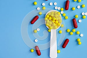 A dosed spoon filled with yellow vitamin C against a background of randomly scattered tablets photo