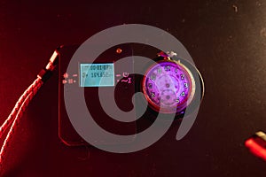 Dosimeter of radioactive radiation and old broken pocket watch with dangerous fluorescent paint. Violet light and green glow of