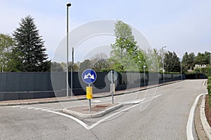 Double arrow traffic sign at the end of a roundabout. Black anti noise panels on the left, empty road, no people