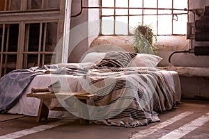 Bed with pillows and blanket, wooden stool and plant in a wabi sabi bedroom photo