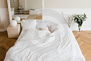 A double bed with white linens and beige pillows in a bright Scandinavian bedroom, a bed on the floor and flowers in a vase