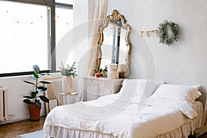 A double bed with white linens and pillows in the bedroom decorated for Christmas and New Year. Christmas wreath near the mirror