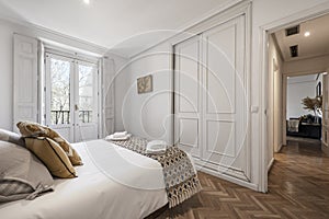 Double bedroom with beautiful decoration in hardwood, white fitted wardrobes, matching blanket and cushions, herringbone oak